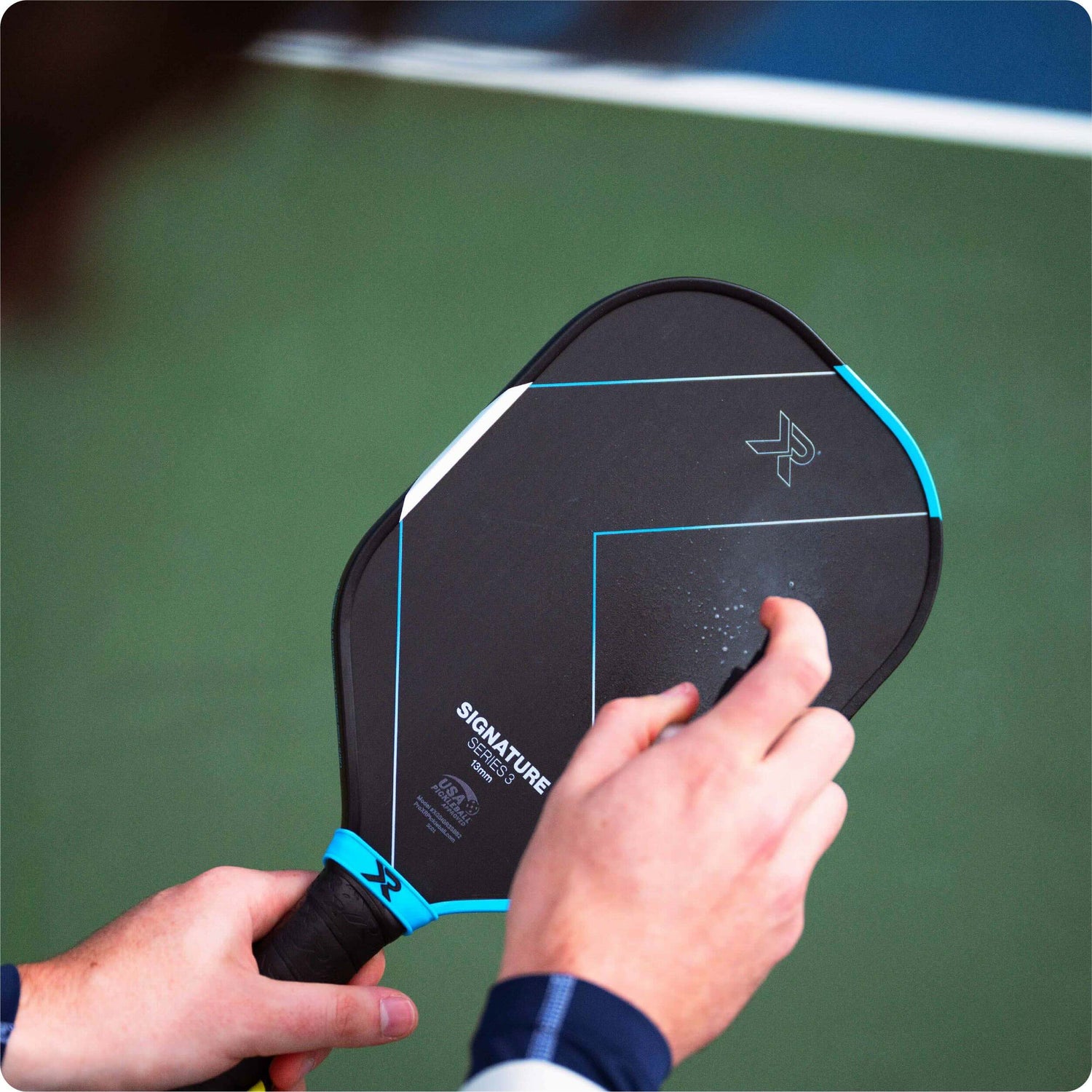 person spraying pickleball paddle with RESET pickleball paddle cleaner against a blurry court background