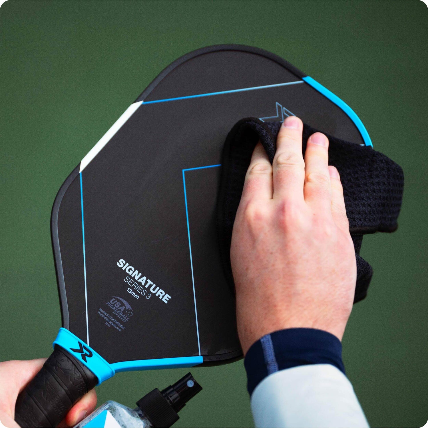 person wiping a pickleball paddle with a cloth against a green background