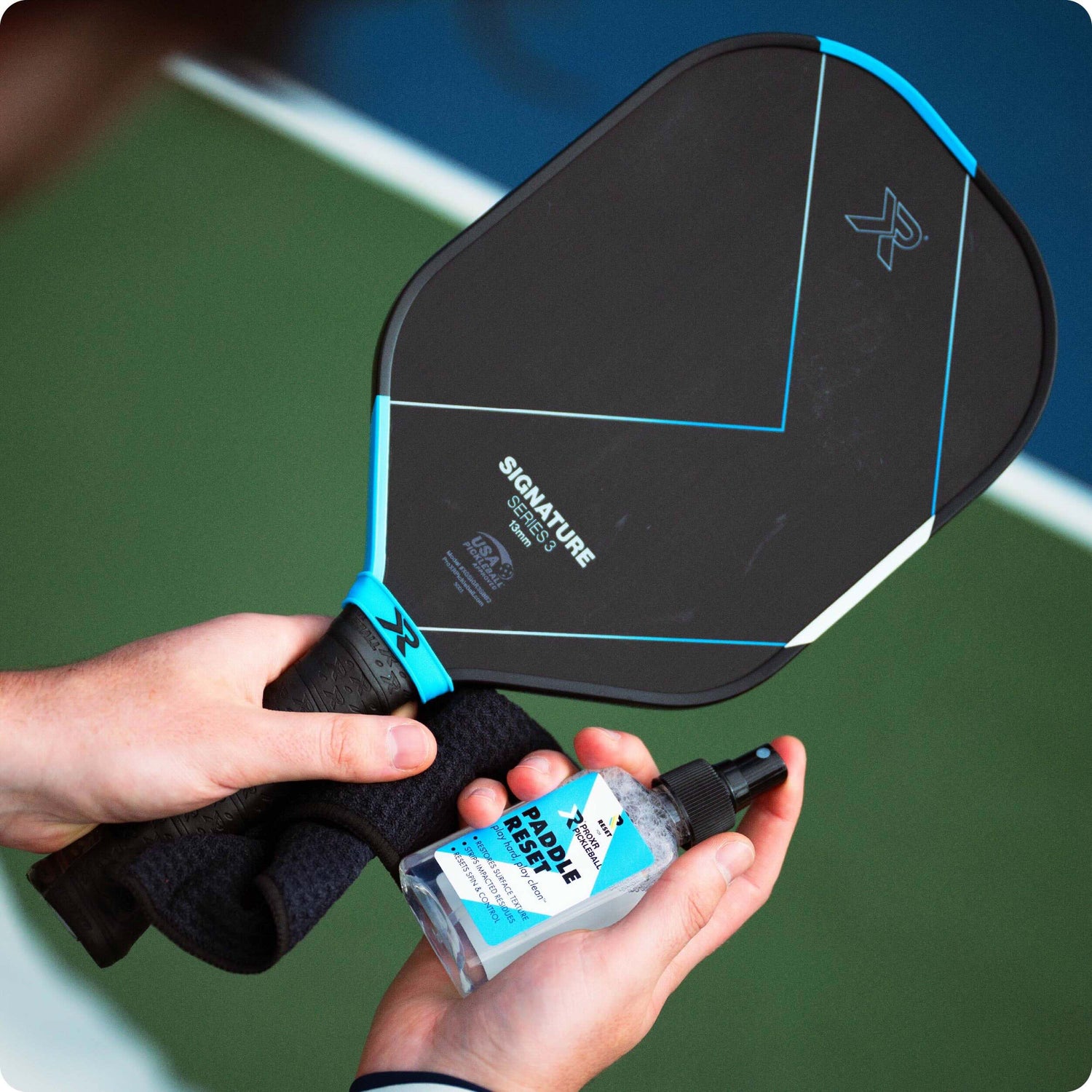 person holding pickleball paddle and RESET pickleball paddle cleaner against a blurry court background