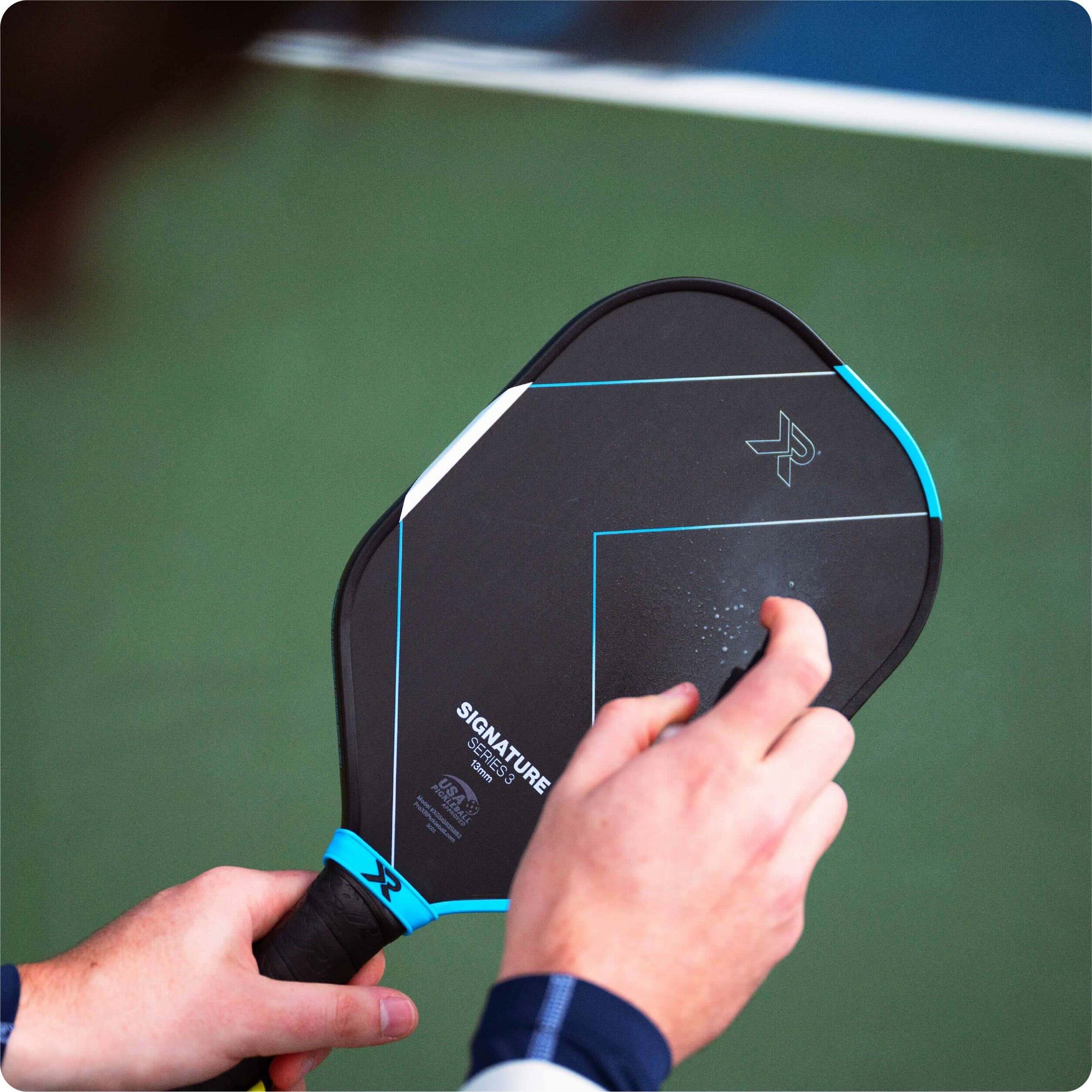 person spraying pickleball paddle with RESET pickleball paddle cleaner against a blurry court backgroundmain